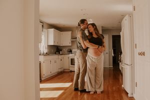 A couple embraces while standing in their bright modern kitchen with white cabinets and hardwood floors.