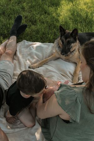A person and a German Shepherd dog relax together on a blanket in the grass on a sunny day.