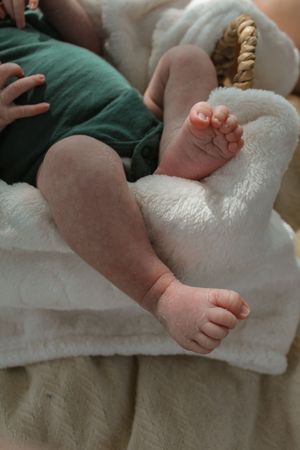 Close-up of tiny bare baby feet and legs resting on white fluffy blankets.