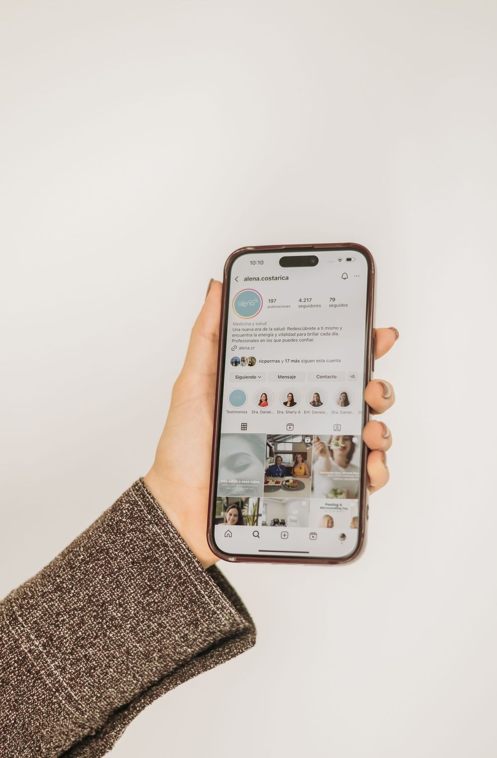 Hand holding iPhone showing Instagram social media app interface with posts and stories against white background.