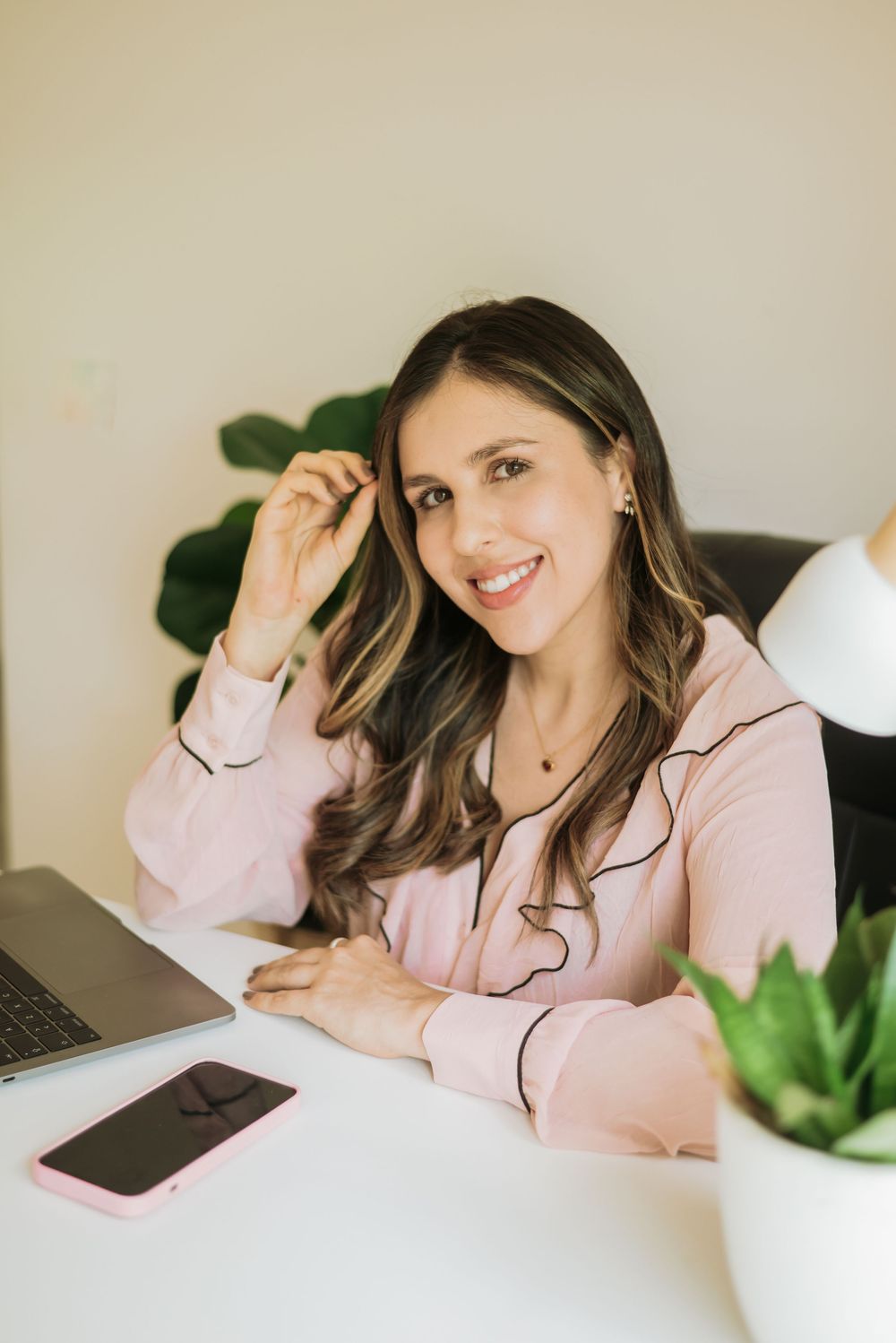 Person in a pink blouse working at desk with laptop and plants, showcasing a casual home office setting.
