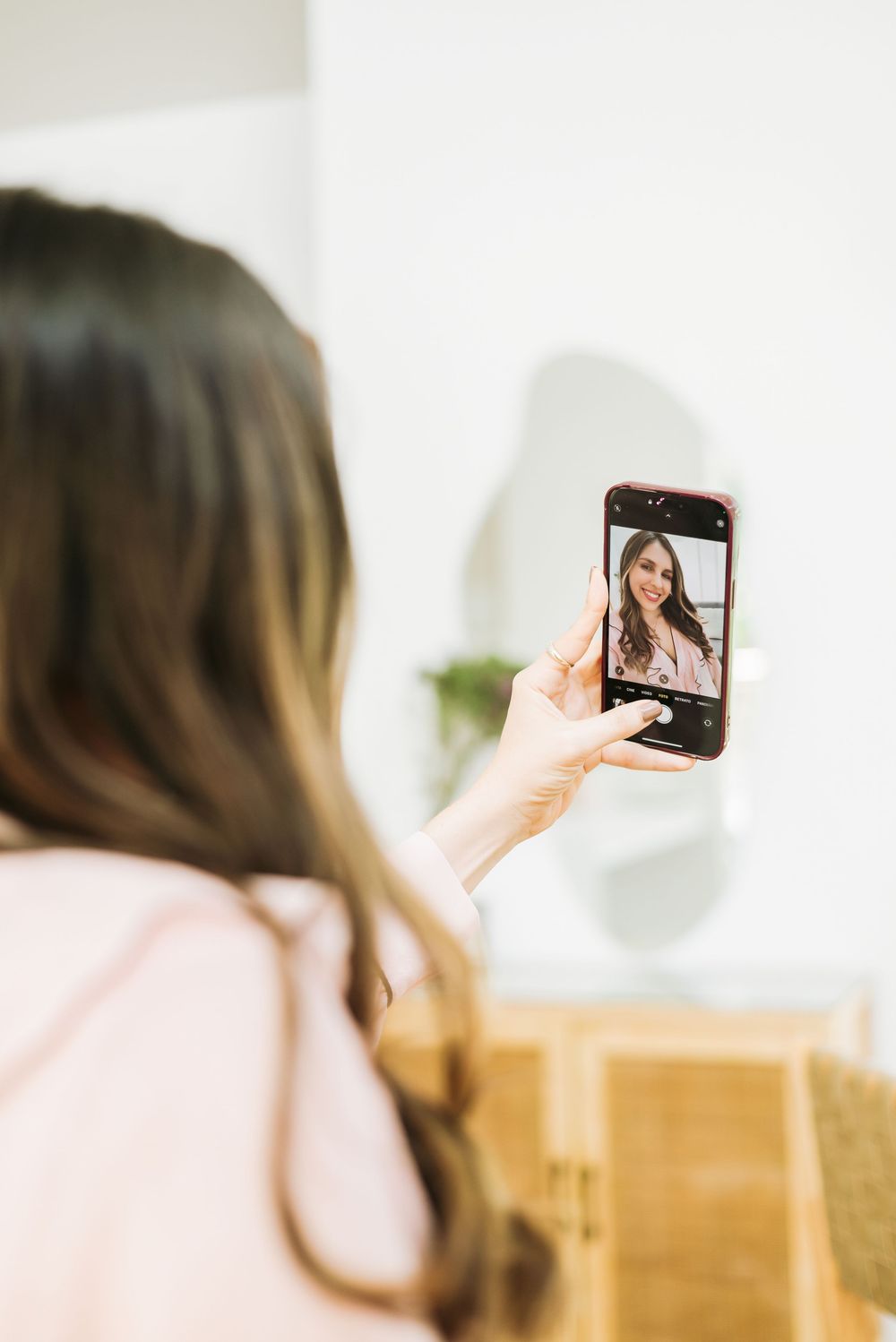 A person takes a selfie with a smartphone showing their reflection in a photo composition.