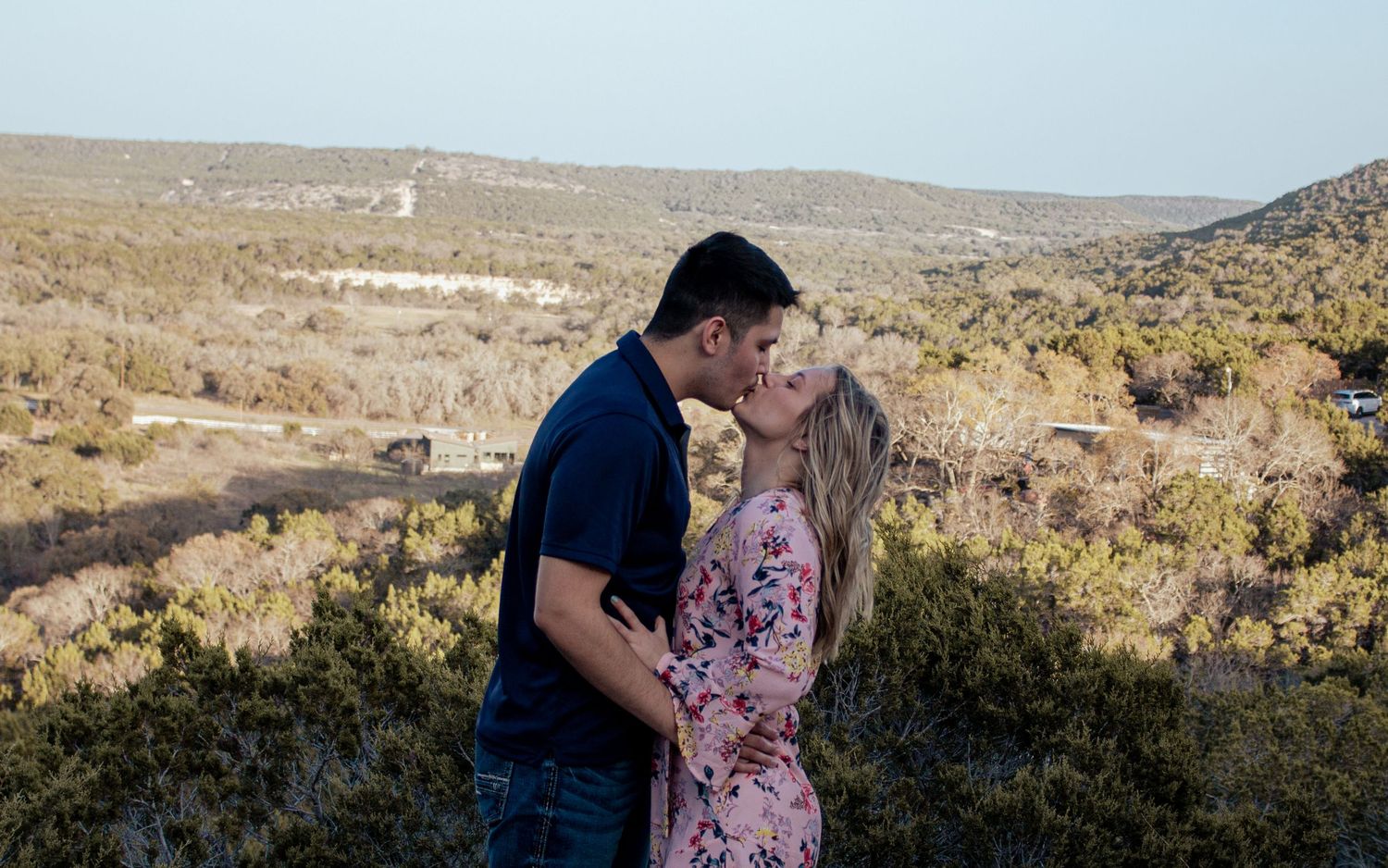 A couple shares an intimate moment while standing on a hill overlooking a desert landscape during golden hour.
