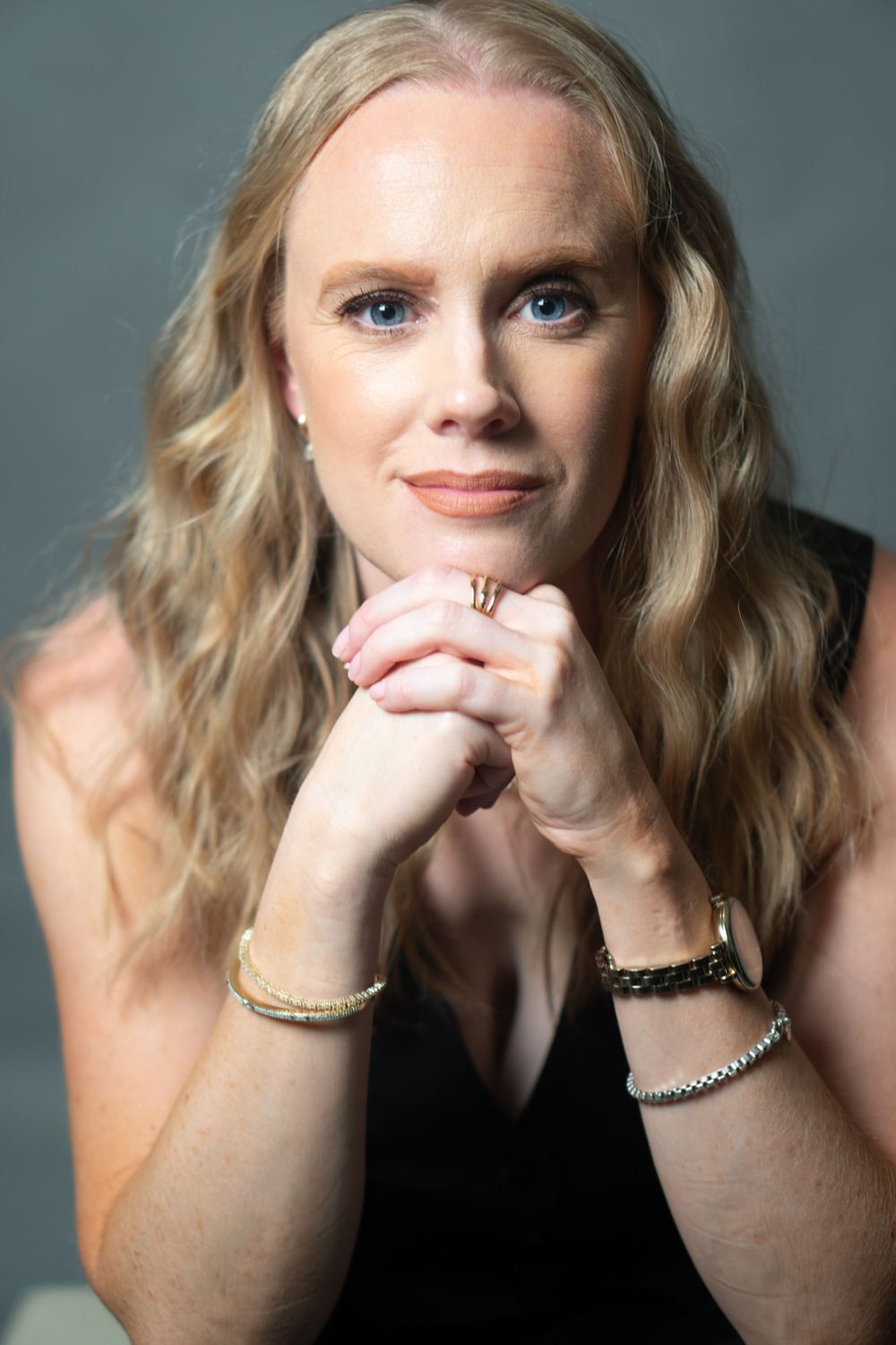 Elegant studio portrait with wavy blonde hair wearing black top and jewelry.