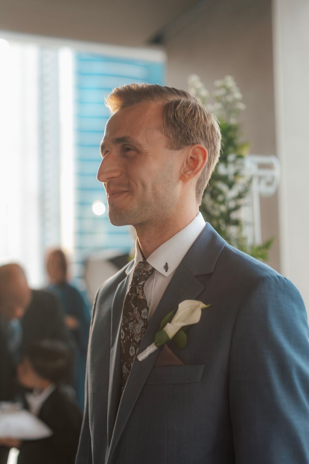 Groom wearing navy suit with floral boutonniere at wedding ceremony.