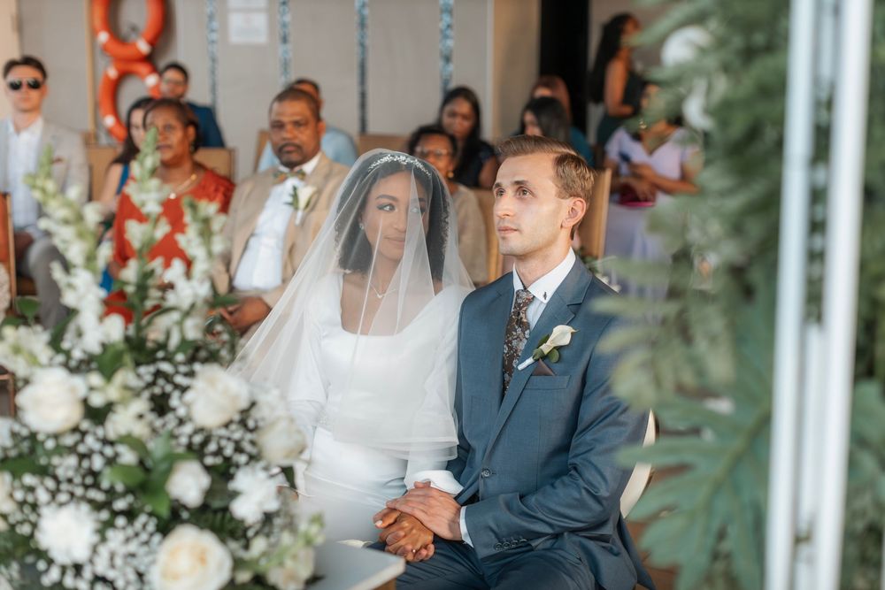Elegant wedding ceremony scene with white floral decorations in bright indoor venue.