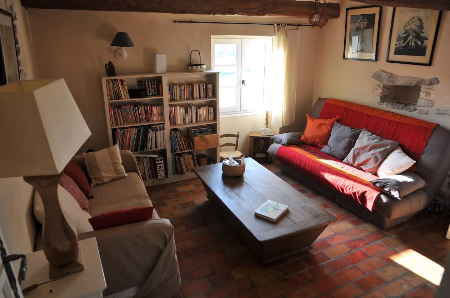 A cozy living room with bookshelves, red couch, and rustic coffee table bathed in natural sunlight.