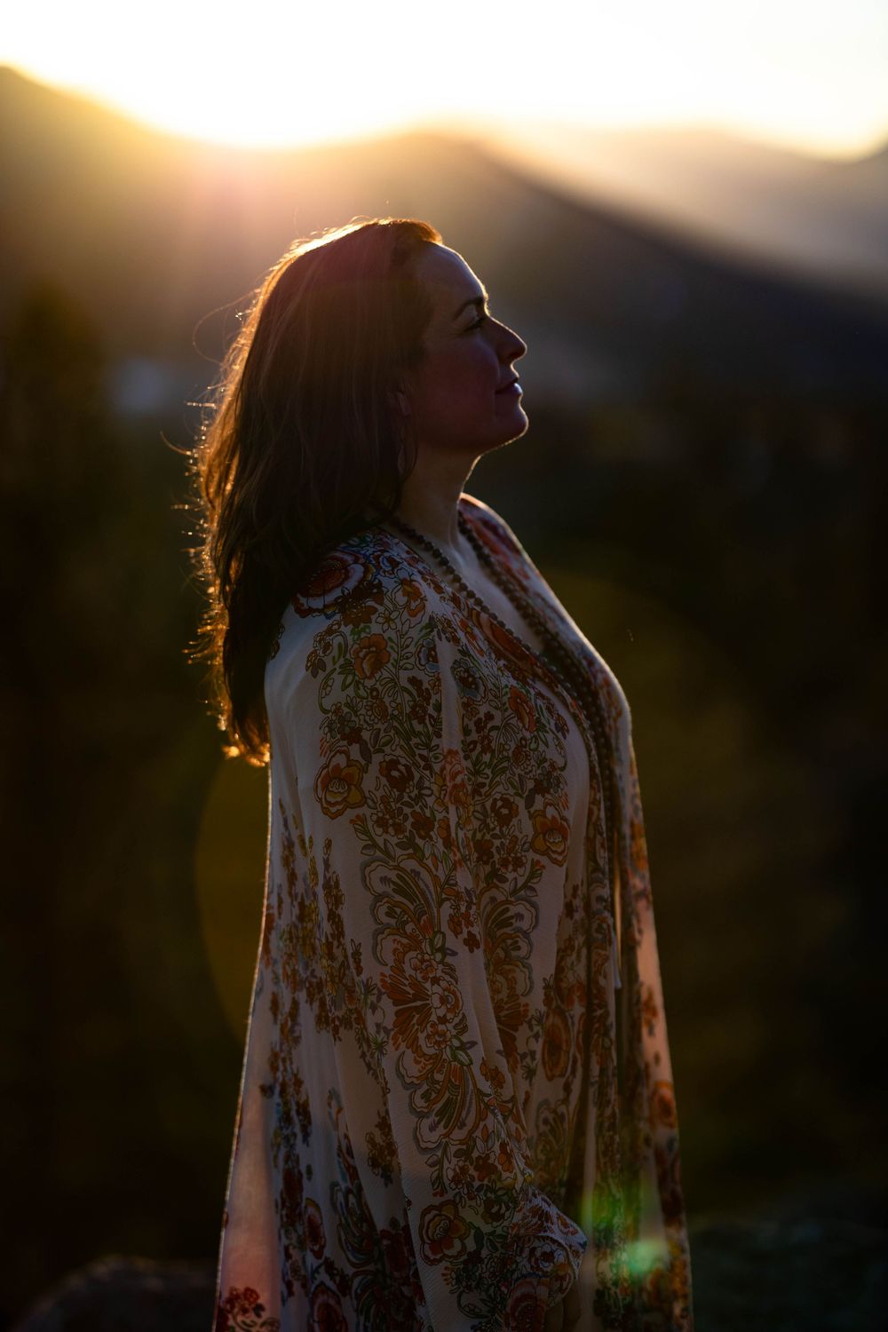 Silhouette of person in patterned robe standing against golden mountain sunset.