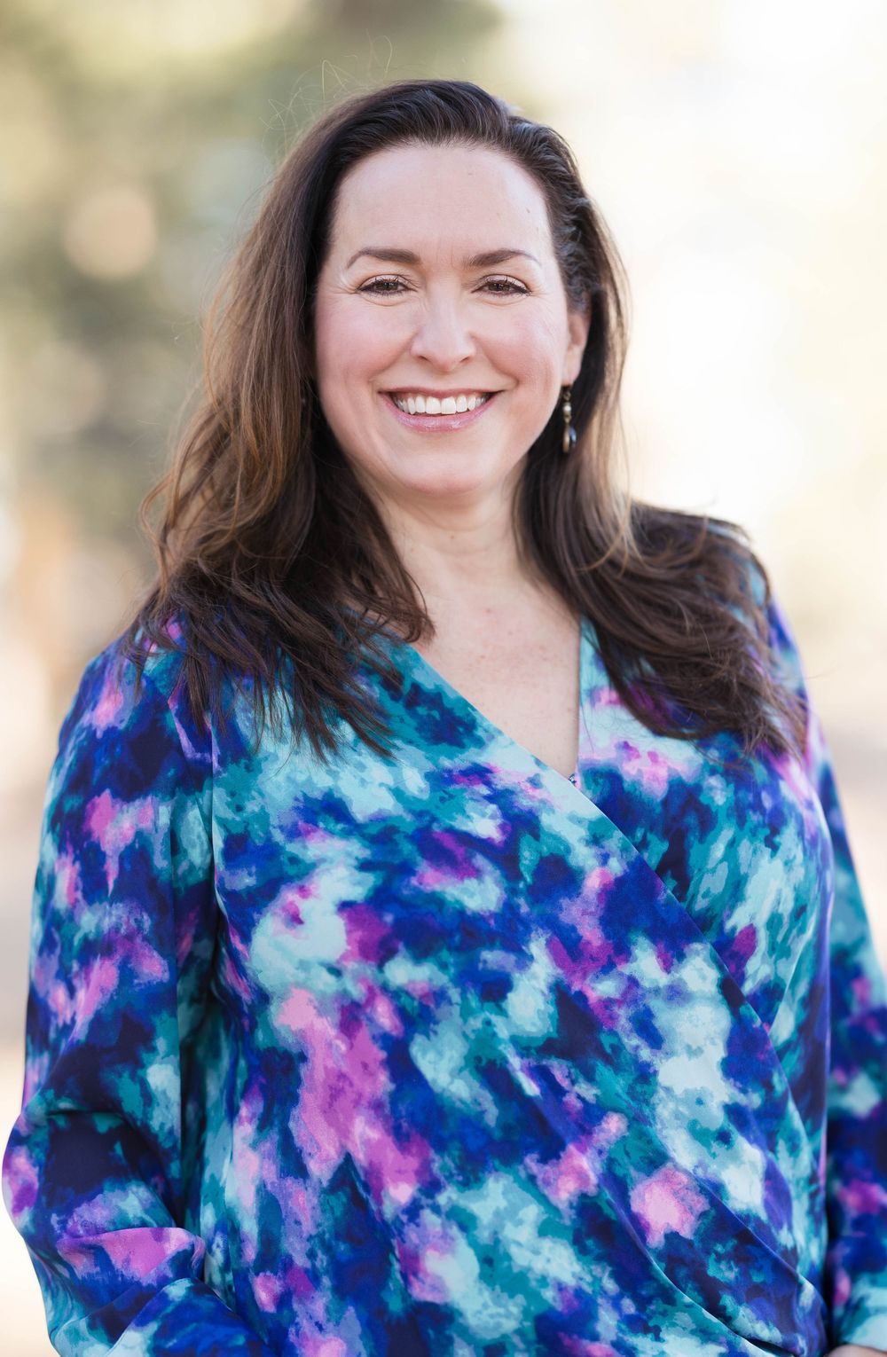 A person in a vibrant blue and purple tie-dye pattern top stands against a soft blurred background.