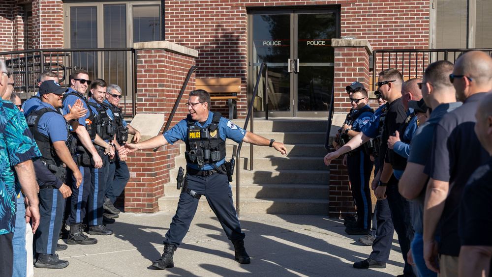 Law enforcement officers receive training and instructions during an outdoor demonstration at a brick building entrance.