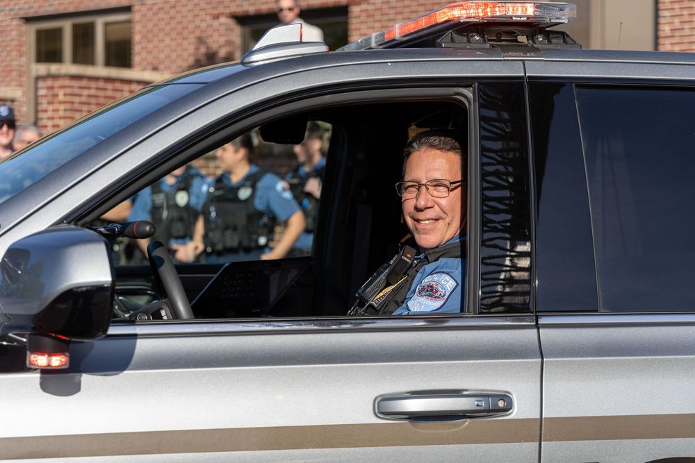 Uniformed officer smiles while sitting in the driver's seat of a police patrol vehicle.