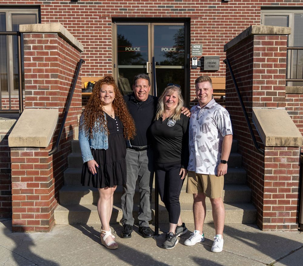 A group of four people standing together outside a brick building entrance on a sunny day.
