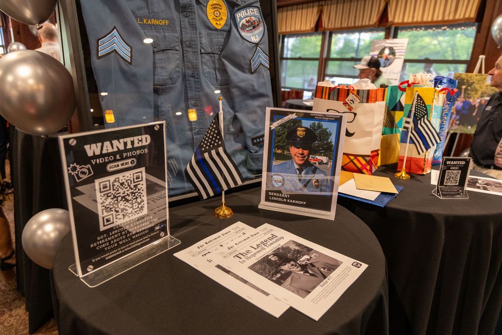 Display table with wanted posters and police uniform at an event decorated with black balloons and tablecloths.