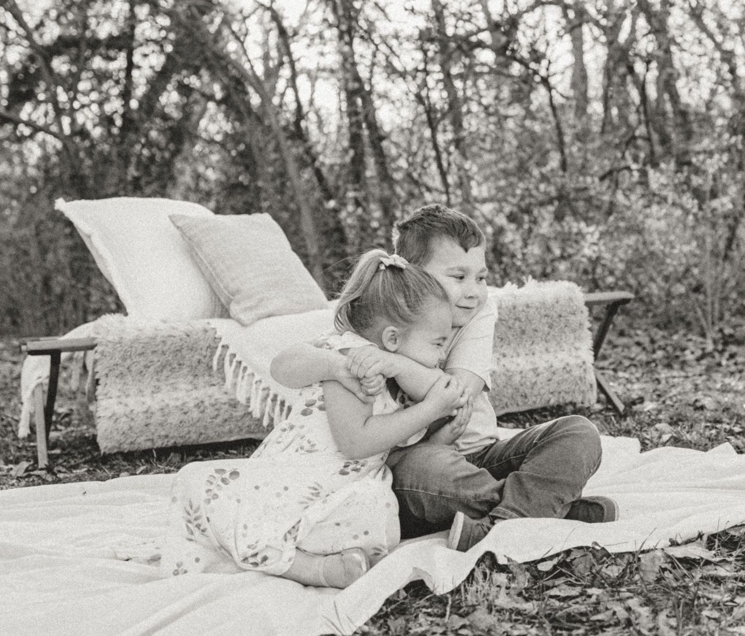 Two children sitting on a blanket with pillows outdoors reading a book together on a cozy afternoon.