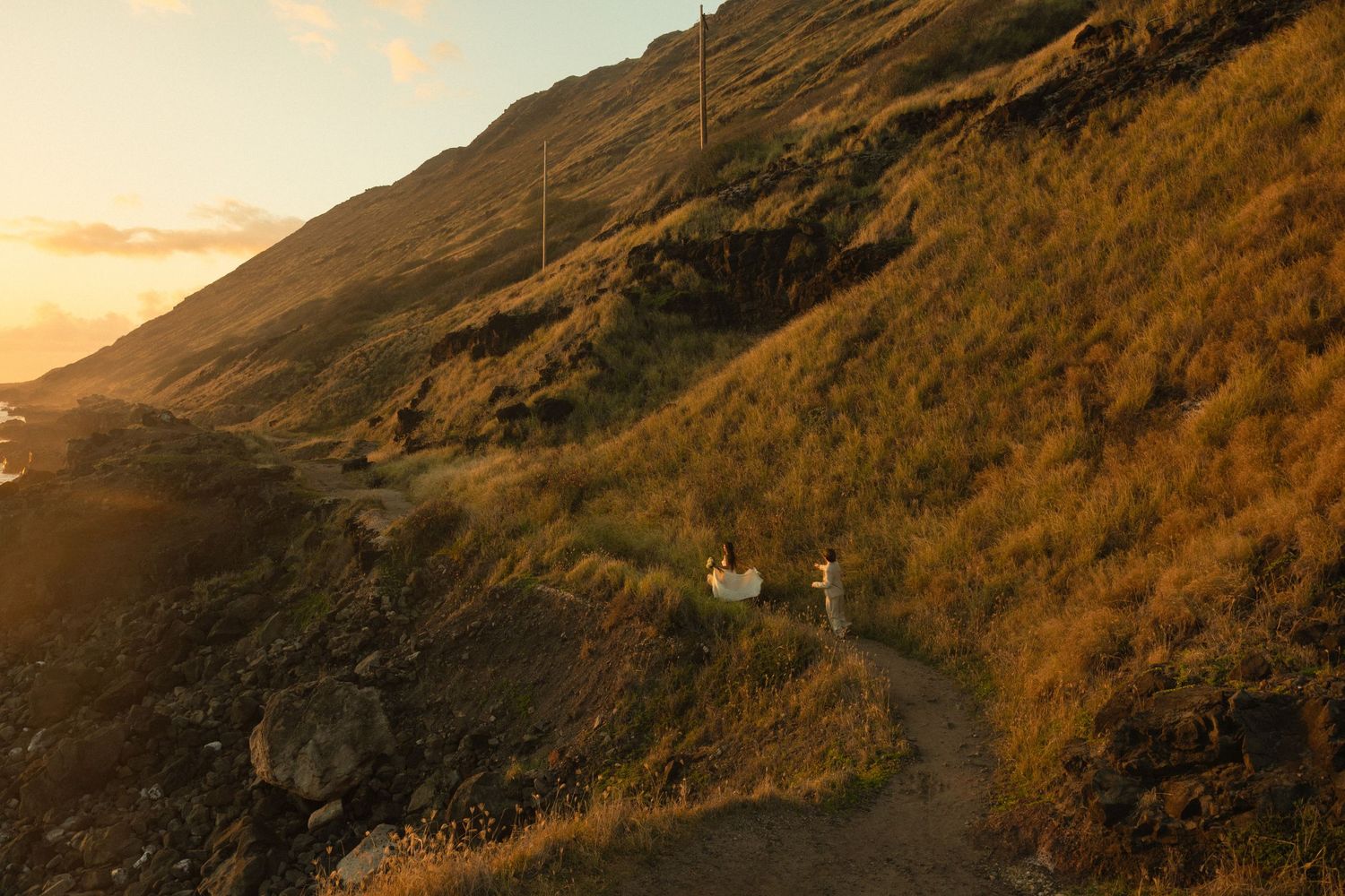 Winding mountain road along a rocky cliff at golden sunset with dramatic lighting illuminating the rugged landscape.