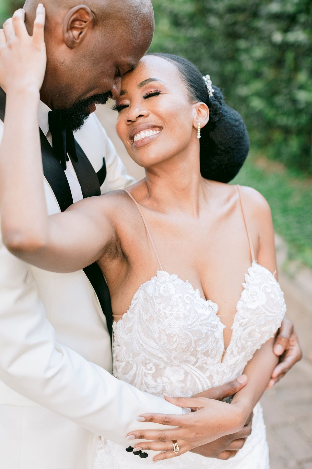 Elegant Black bride and groom sharing an intimate forehead touch, bride wearing a beaded sweetheart gown outdoors.