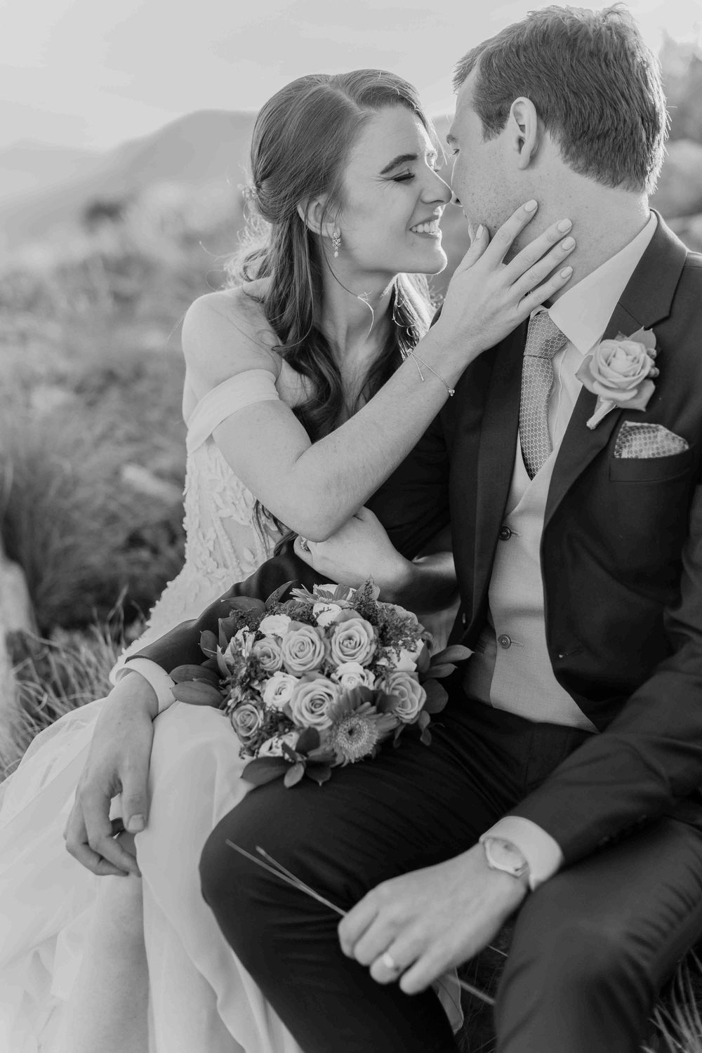 Black and white photo of bride and groom sharing an intimate moment, bride holding bouquet of roses.