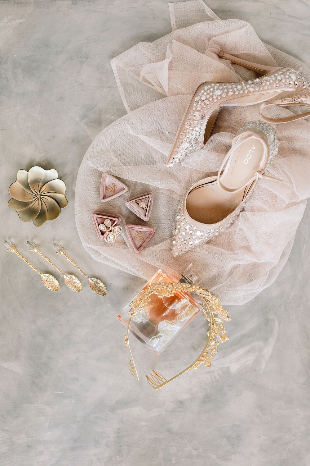 Flat lay of pearl-embellished bridal heels, gold tiara, earrings, and ring boxes on soft tulle fabric.