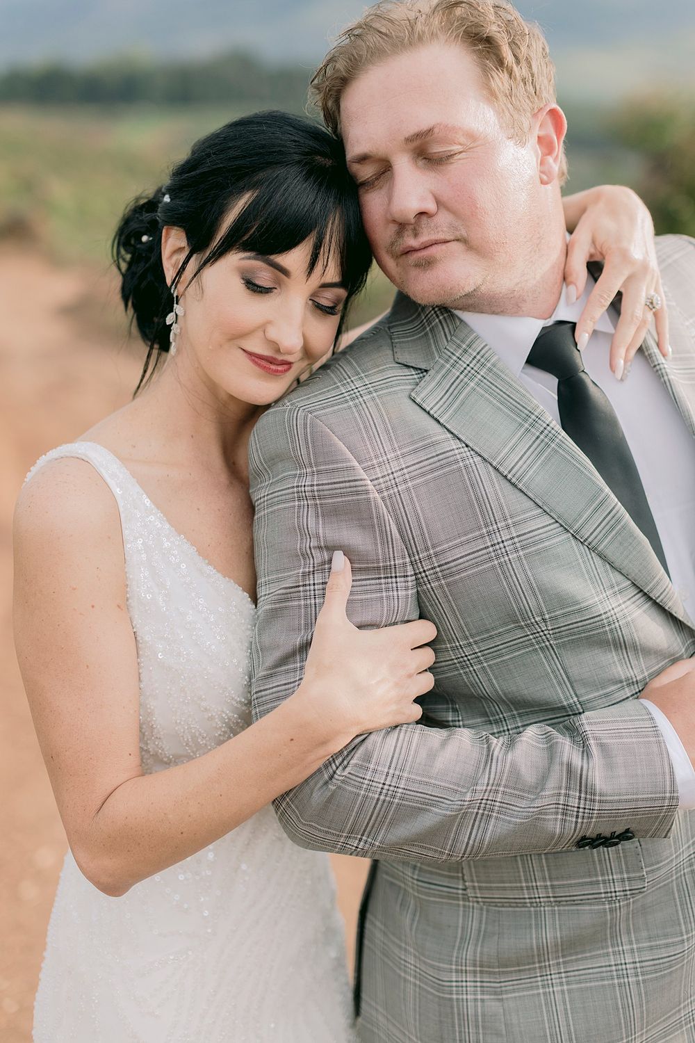 Bride and groom sharing tender embrace on rustic dirt road with mountain backdrop at wedding.