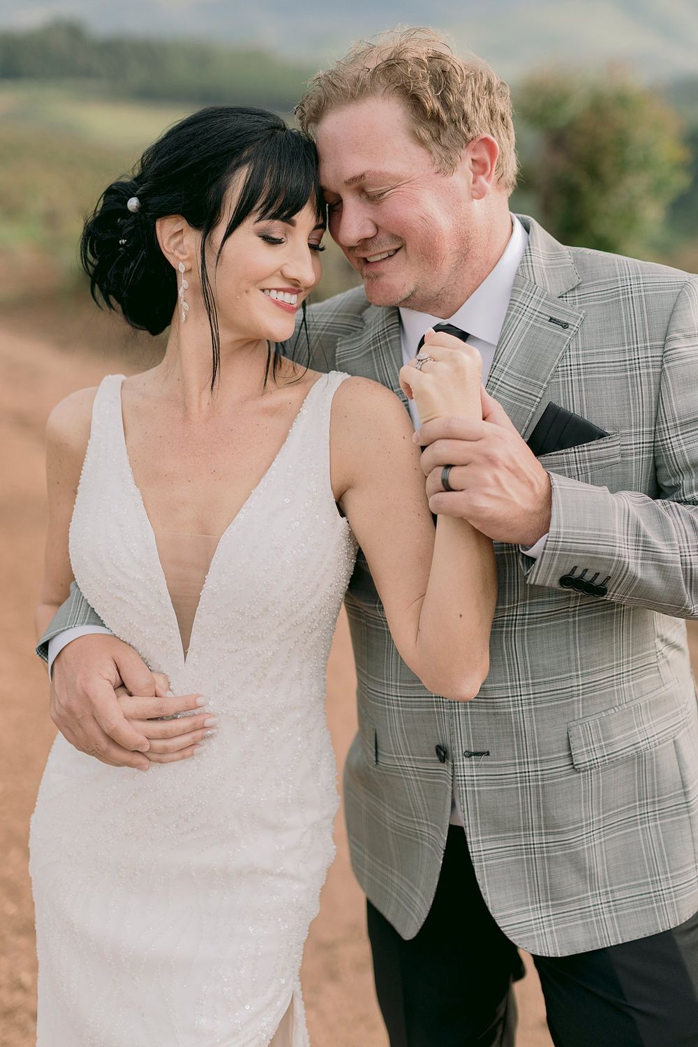 Bride and groom laughing together holding hands on scenic dirt road during wedding photo session.