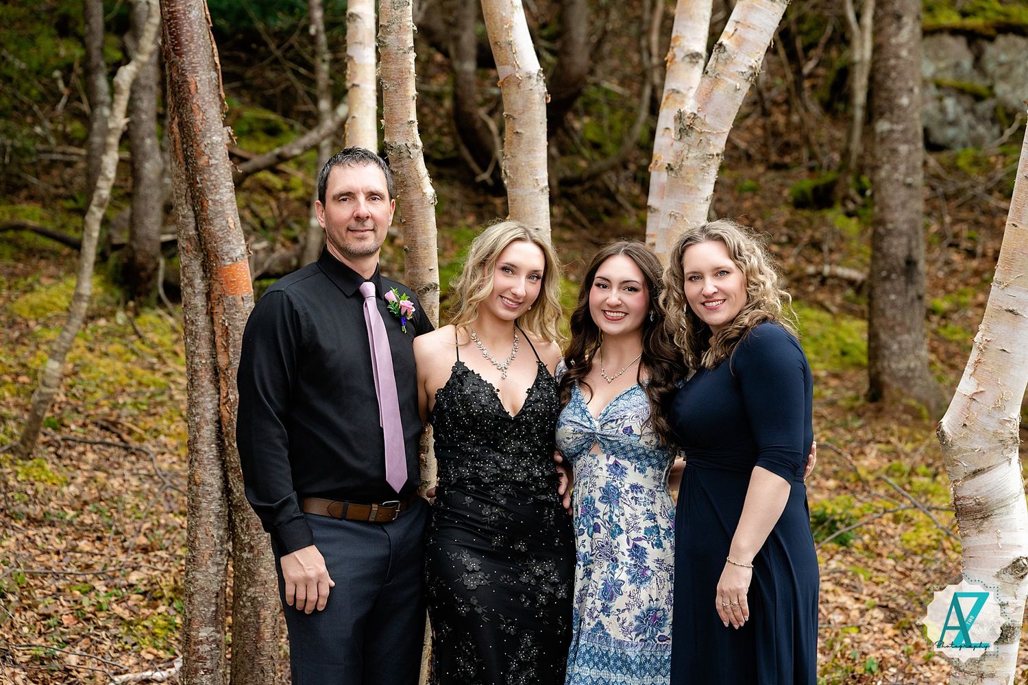 A group of four people pose together in formal attire among birch trees in a forest setting.
