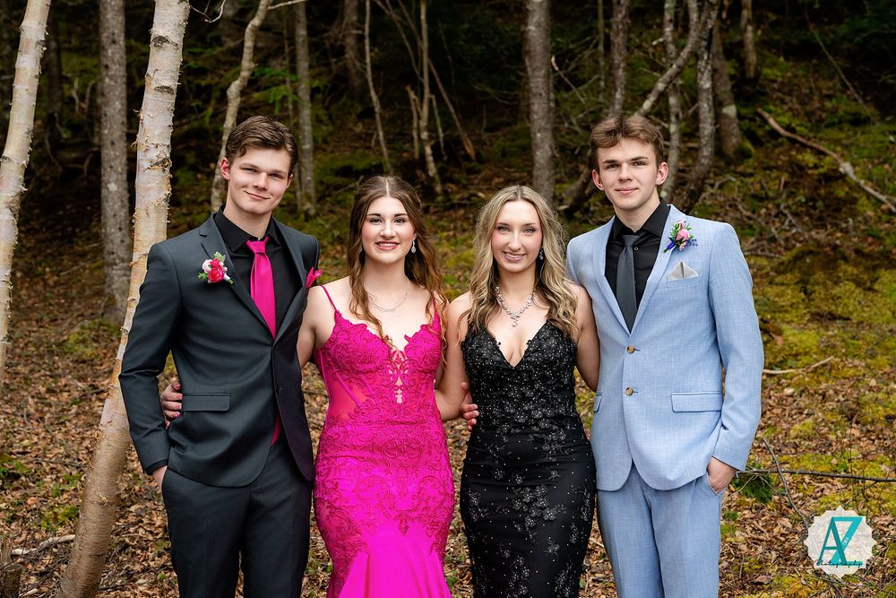 Four people in formal attire pose together in a wooded outdoor setting wearing prom dresses and suits with boutineers.