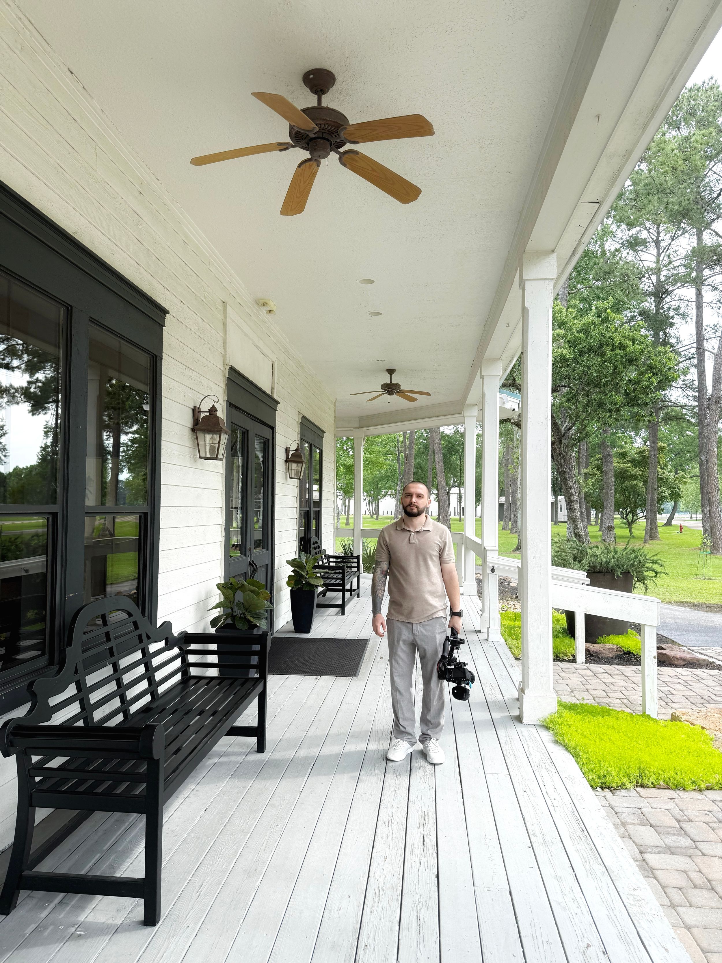 White colonial porch with black benches, ceiling fans, and tall columns overlooking a green landscaped lawn.