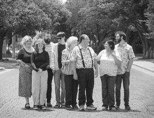 Black and white photo of a group of eight people standing together outdoors on a brick path surrounded by trees.