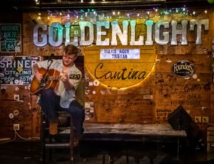 Illuminated golden neon bar sign glows against rustic exposed brick wall in dimly lit establishment.