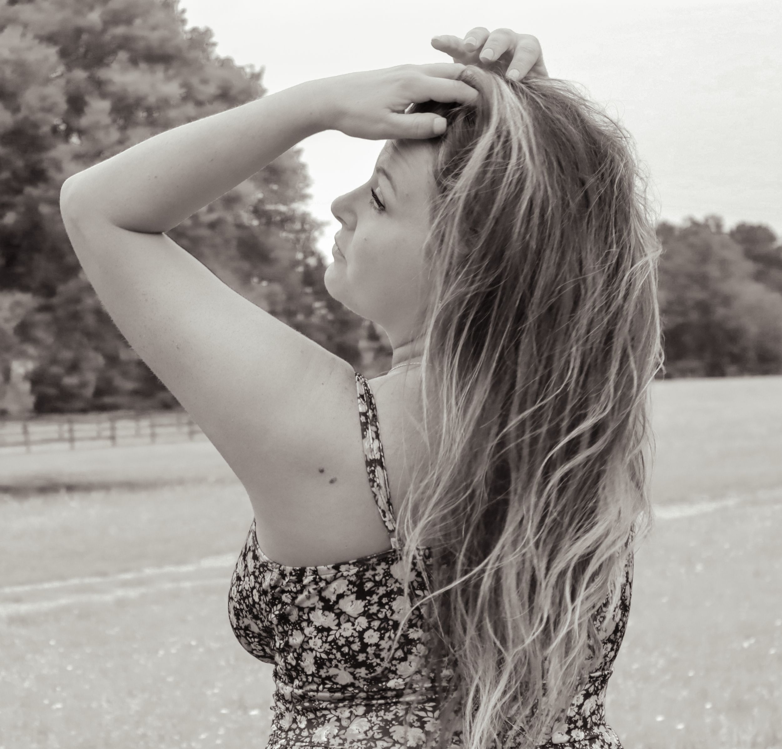 Black and white portrait shot of long-haired person in floral dress outdoors in a park setting.