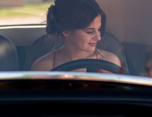 A passenger in a car smiles while looking down, illuminated by soft natural light streaming through the window.