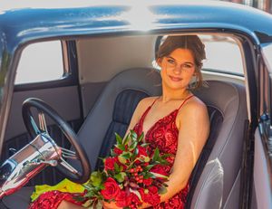 A classic vintage car interior with gray seats, featuring roses and a red dress.