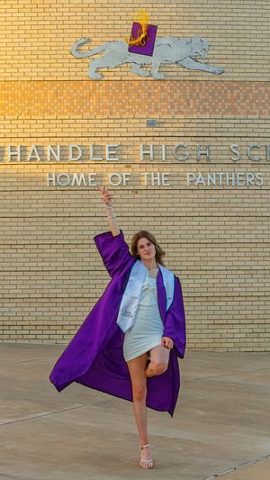 A female graduate in purple cap and gown poses triumphantly outside Panhandle High School Home of the Panthers.