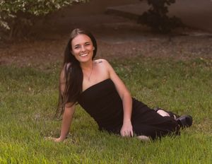 Person in a black dress posing on grass during an outdoor photo session.