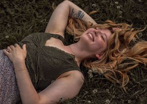 Someone with long strawberry blonde hair lies back on dark ground while laughing joyfully in a black top.
