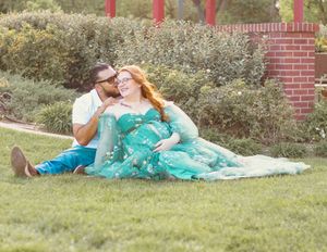 A couple in turquoise outfits relaxes together on a blanket in a grassy outdoor setting during a photo session.