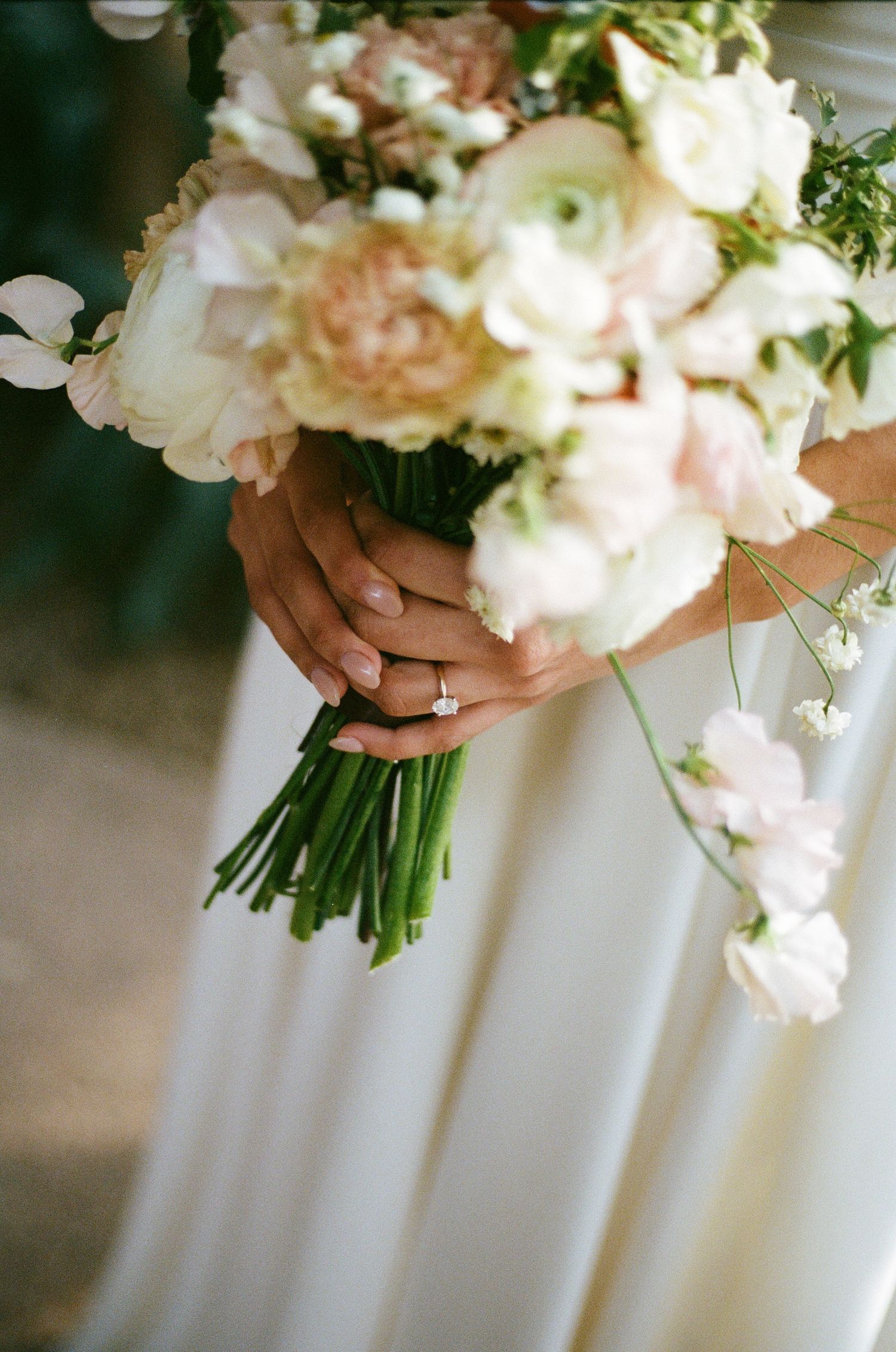 Close-up of hands holding an elegant white and blush wedding bouquet with roses and delicate greenery.