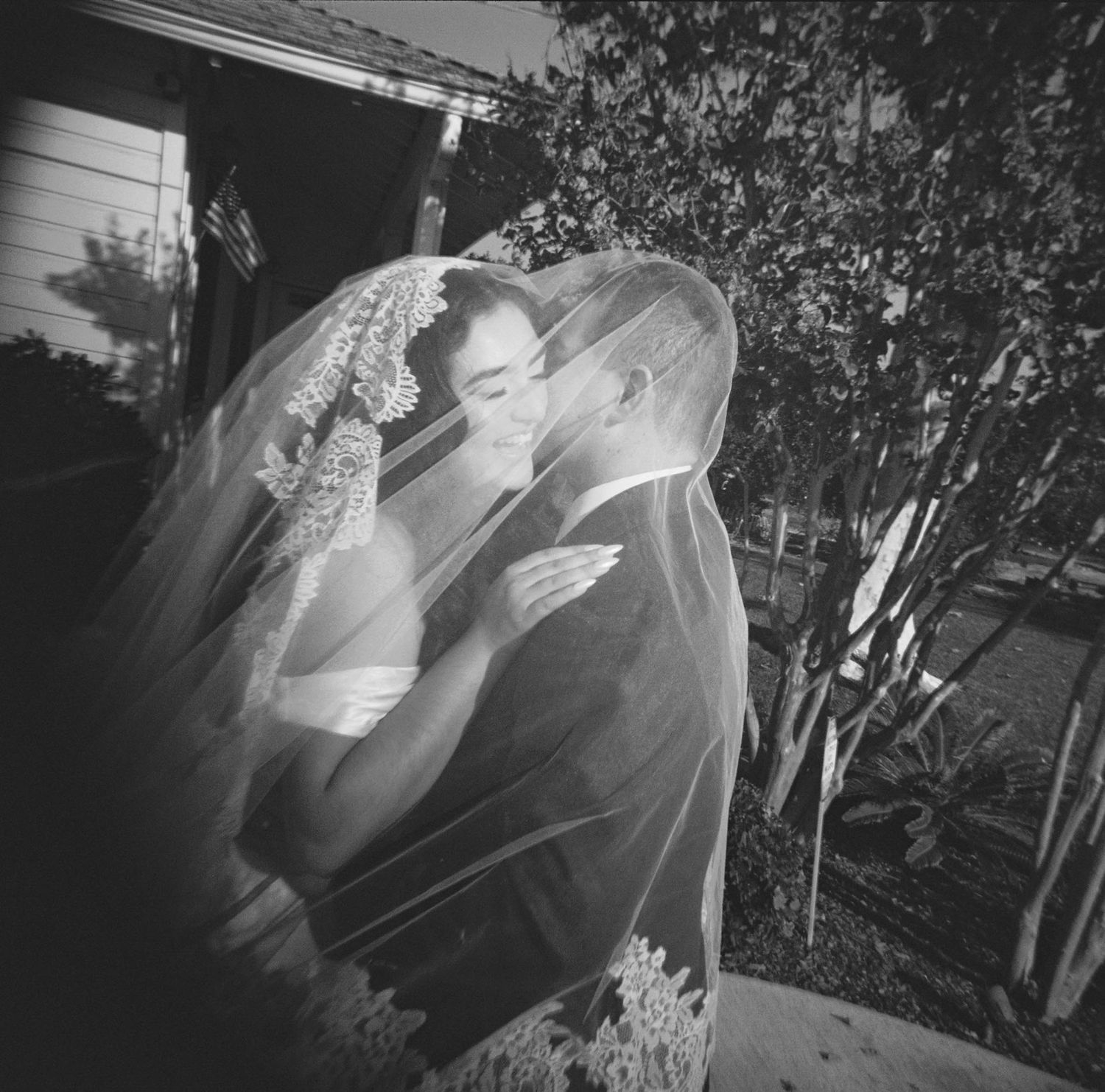 A romantic black and white wedding photo shows a couple sharing a tender moment under a delicate lace veil.