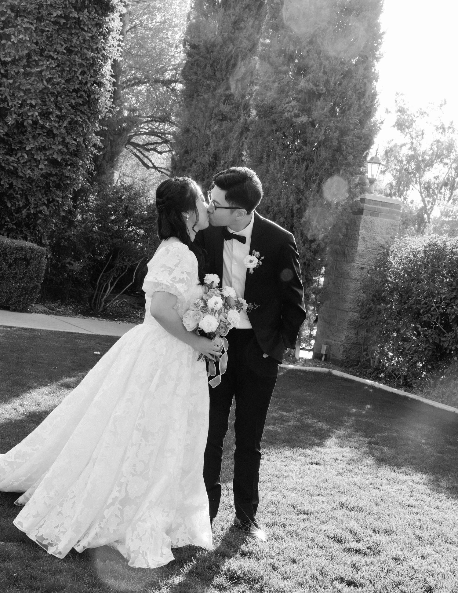 A black and white wedding portrait captures a couple sharing a romantic moment in a garden setting.