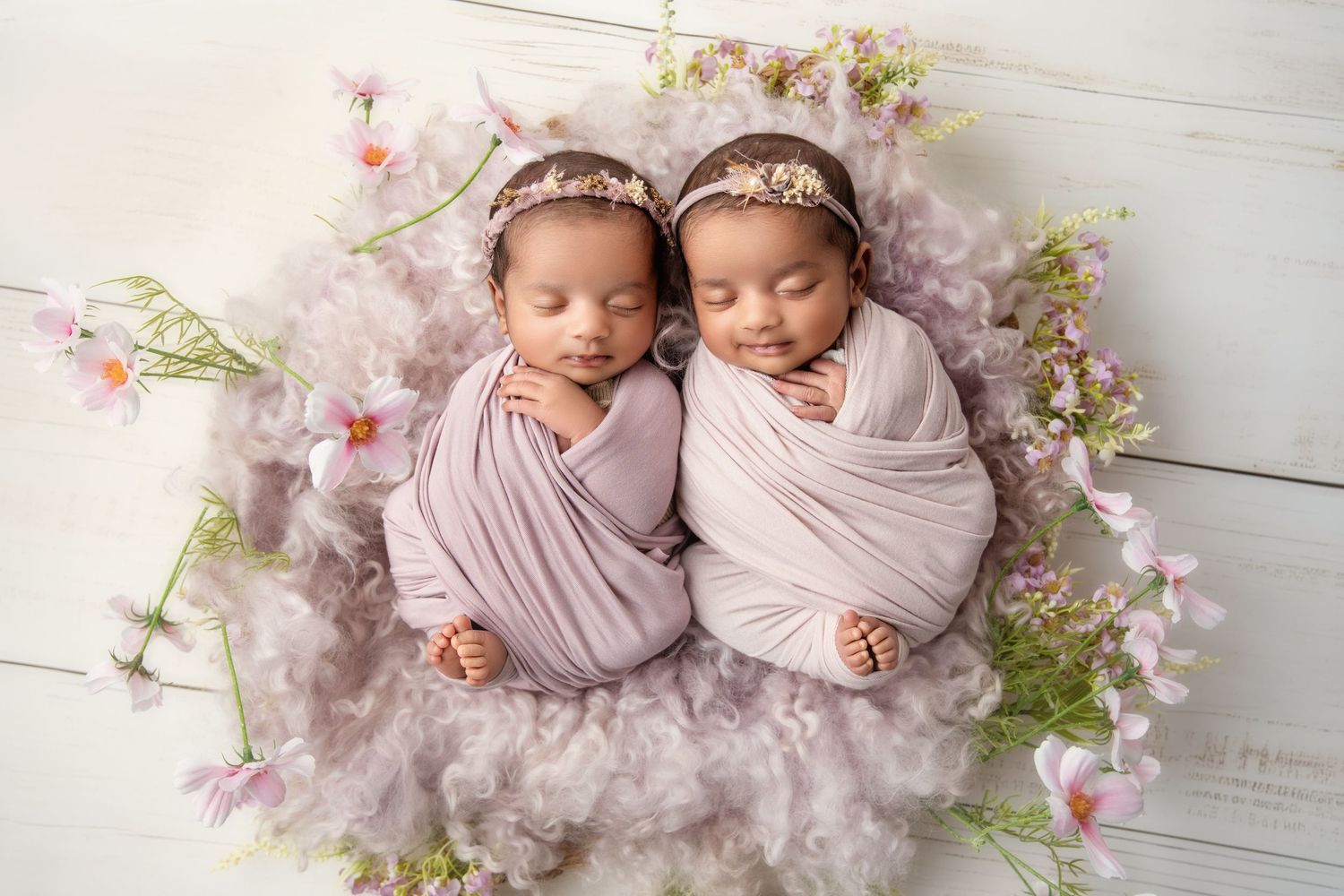 Delicate twin newborn photography setup with pink cherry blossoms and soft wraps.