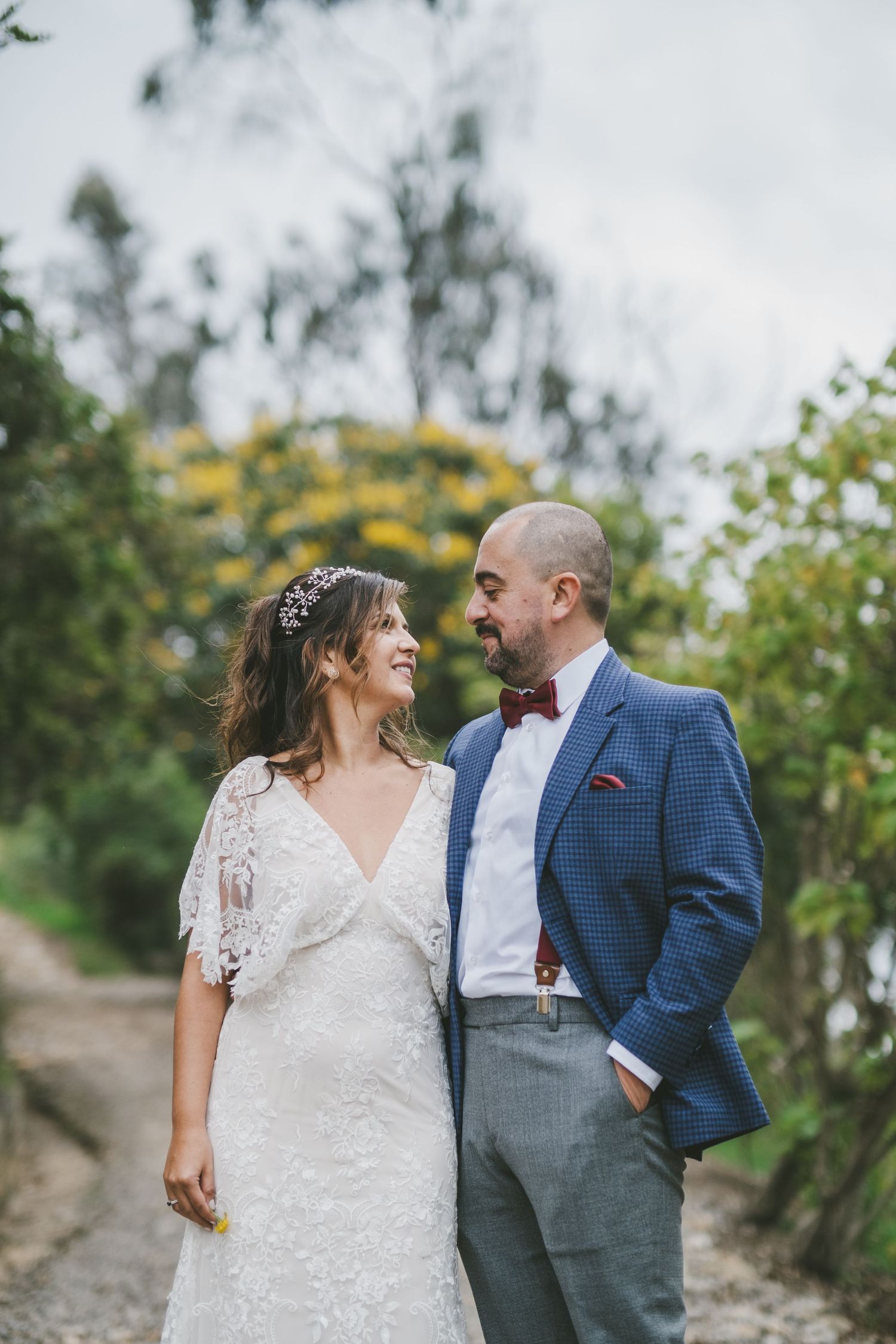 A couple in wedding attire share a romantic moment on a gravel path surrounded by green foliage.