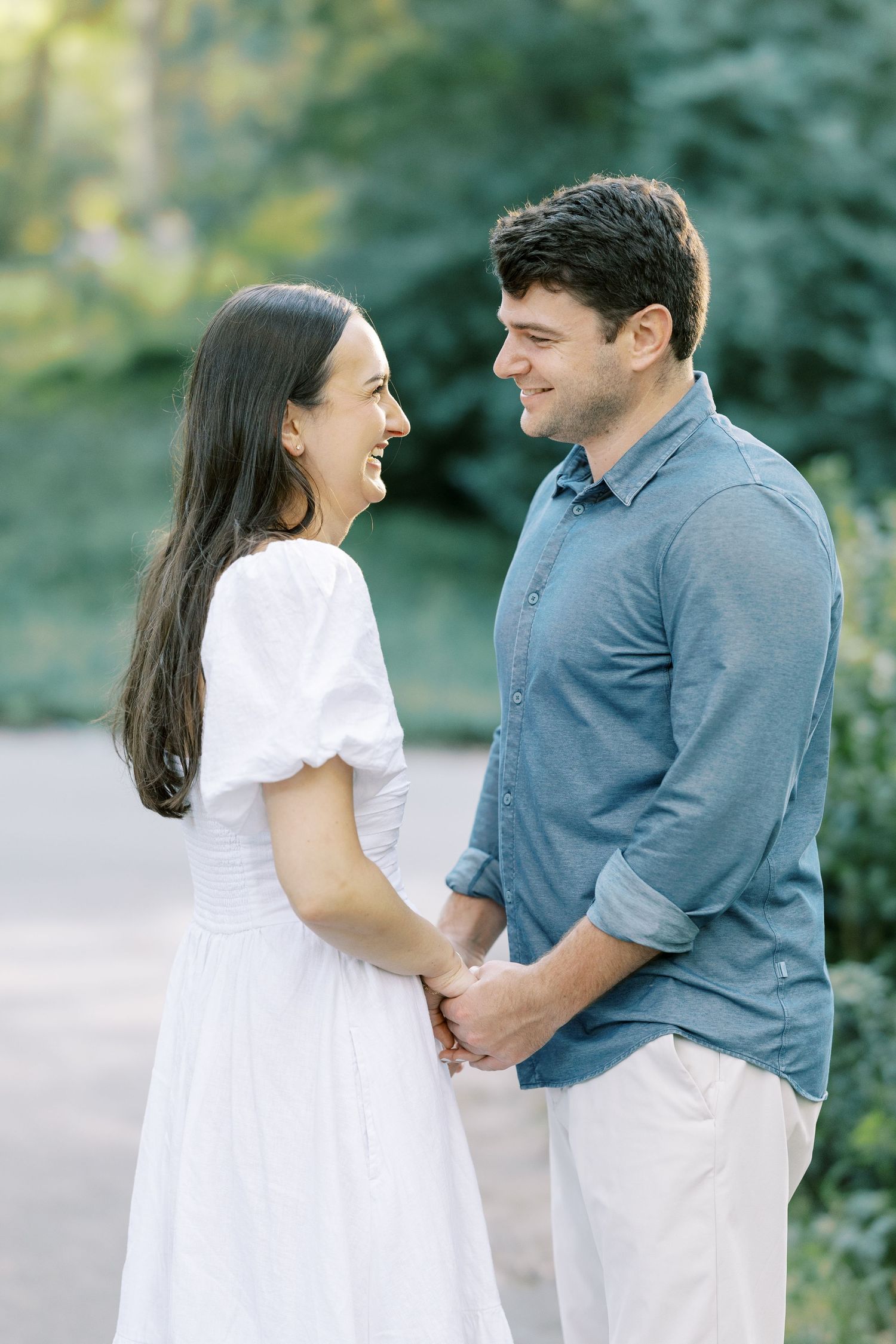 A couple in casual white and blue outfits share playful moments together during an outdoor photo session.