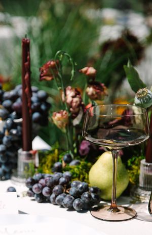 Elegant table setting with wine glasses, fresh blueberries, and pears against a blurred green background.