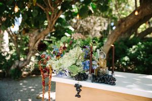 Wedding cake displayed on a decorated table in a lush garden setting with ornate floral arrangements and natural lighting.