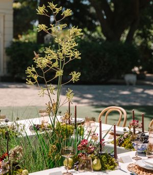 Delicate yellow flower arrangements adorn an outdoor table setting with natural garden elements and glassware.