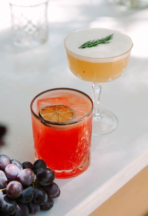 Elegant cocktails garnished with citrus and herbs on a white tablecloth with fresh grapes.