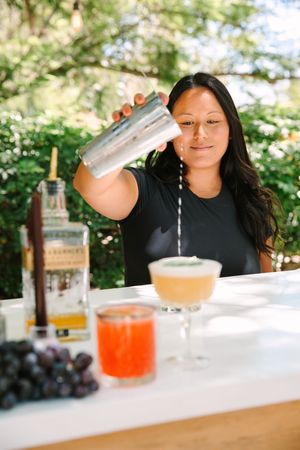Bartender demonstrates cocktail making technique by pouring liquid from shaker into glass with precise control.