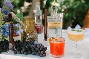 Colorful drinks and cocktails arranged with fresh fruits, flowers and vases on an elegant party table setting with moody lighting.