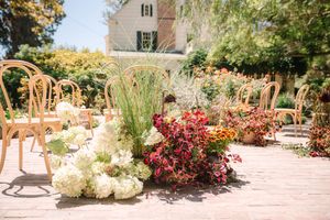 An outdoor garden wedding venue features rustic paths and colorful floral landscaping under bright sunlight.