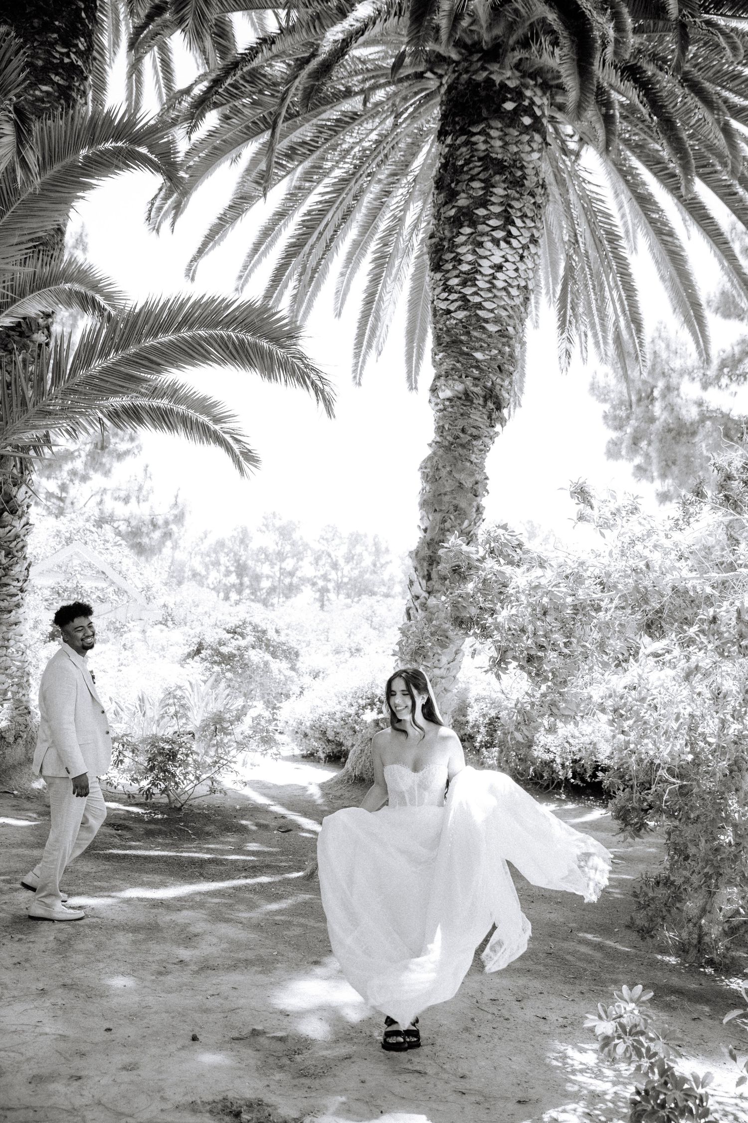 Four black and white photos show figures in long white garments sitting beneath palm trees in a desert oasis setting.